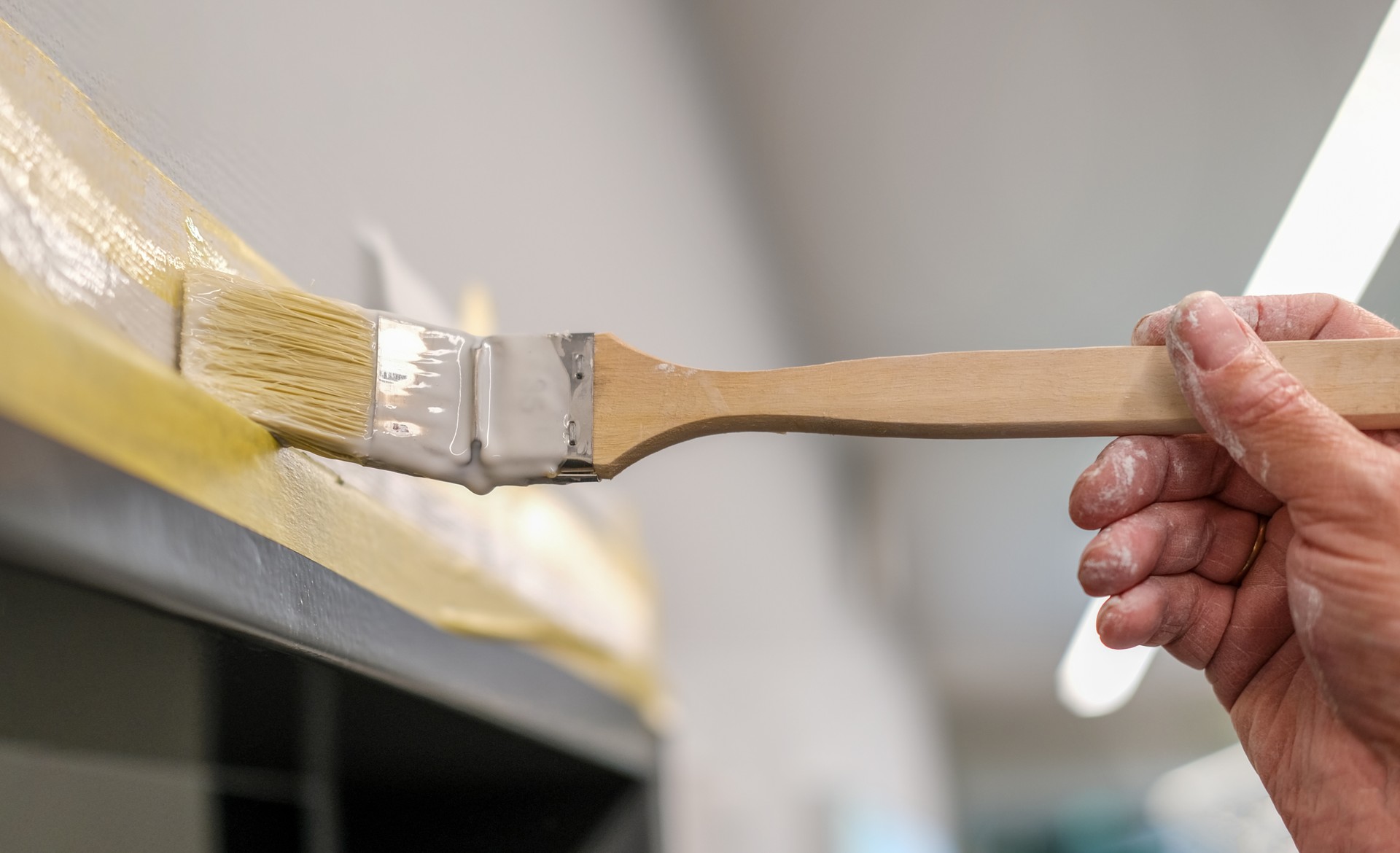 Close-up of a painter's hand painting a door frame with a brush and white paint, selective focus