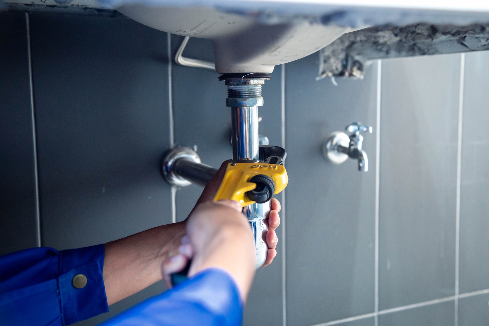 Plumber fixing white sink pipe with adjustable wrench.